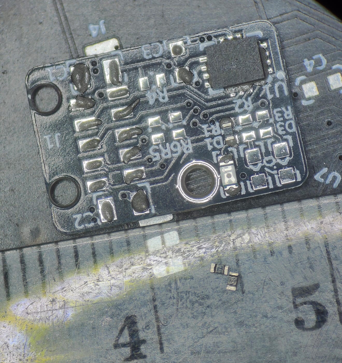 Płytka PCB sensora IMU 10×15 mm przy linijce — układ IMU, rezystory i otwory montażowe